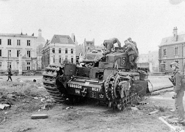 Black and white photograph. Several German soldiers crawl over a Canadian Churchill tank left abandoned in a square in Dieppe. One set of the tank’s tracks has been badly damaged.